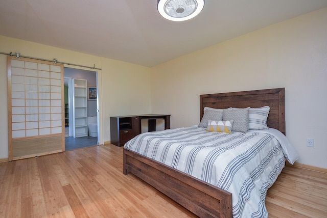 bedroom with light wood finished floors, a barn door, and baseboards