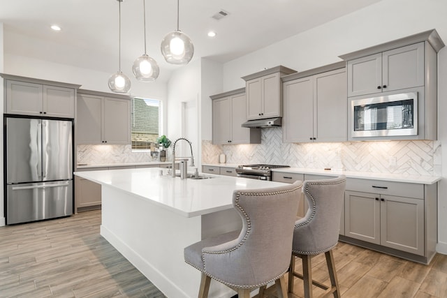 kitchen featuring appliances with stainless steel finishes, gray cabinets, a sink, decorative backsplash, and under cabinet range hood