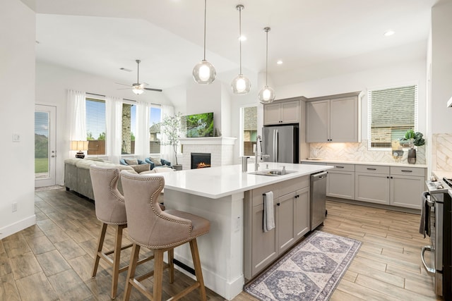 kitchen featuring gray cabinetry, stainless steel appliances, a fireplace, decorative backsplash, and vaulted ceiling