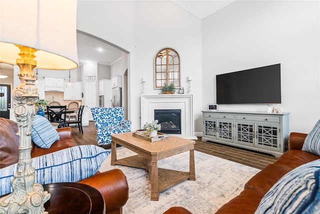 living area featuring crown molding, a towering ceiling, dark wood-style flooring, and arched walkways