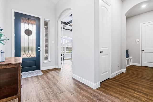 foyer entrance with wood finished floors, baseboards, and arched walkways