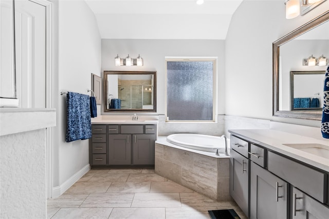bathroom with a sink, lofted ceiling, a stall shower, two vanities, and a garden tub