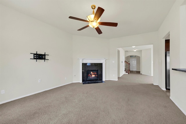 unfurnished living room with a ceiling fan, baseboards, carpet flooring, arched walkways, and a fireplace