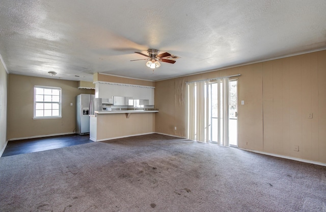 unfurnished living room featuring a textured ceiling, dark colored carpet, baseboards, and a ceiling fan