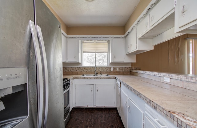 kitchen with a sink, stainless steel appliances, a textured ceiling, dark wood-style flooring, and white cabinetry