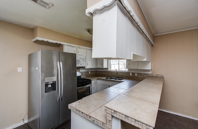 kitchen featuring baseboards, visible vents, a sink, a peninsula, and appliances with stainless steel finishes