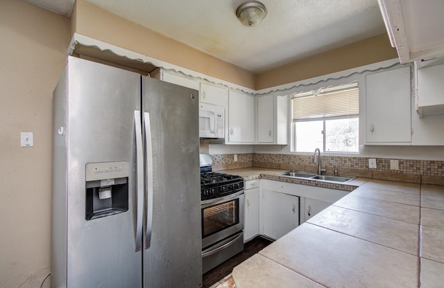 kitchen with a sink, white cabinetry, backsplash, light countertops, and appliances with stainless steel finishes