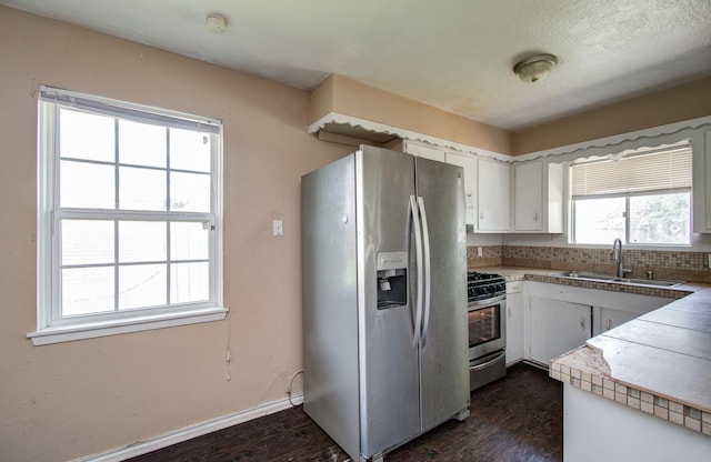 kitchen featuring a sink, stainless steel appliances, dark wood-style flooring, white cabinets, and baseboards