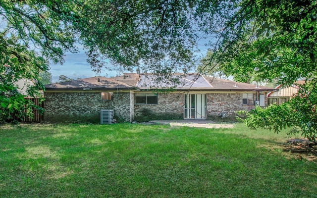 back of house featuring central AC unit, fence, brick siding, and a lawn