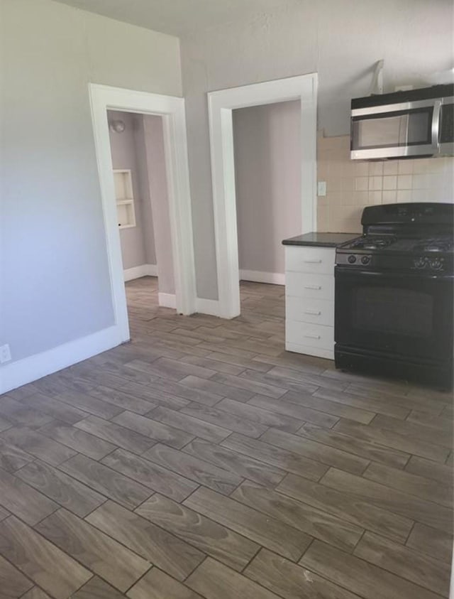125 Canton St, Houston, TX 77012 - kitchen with dark wood finished floors, stainless steel microwave, decorative backsplash, black range with gas stovetop, and dark countertops