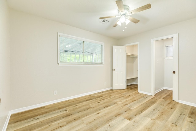 unfurnished bedroom with visible vents, light wood finished floors, a spacious closet, a ceiling fan, and baseboards