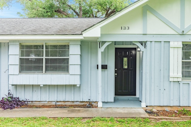 view of exterior entry featuring board and batten siding and roof with shingles