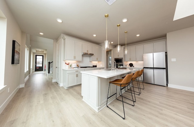 18715 Brego Ln, Tomball, TX 77377 - kitchen featuring stainless steel appliances, a sink, light countertops, a kitchen island with sink, and light wood-type flooring