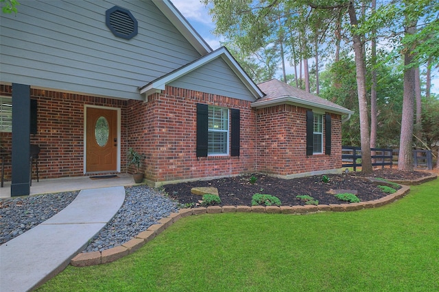 doorway to property featuring brick siding, a yard, and fence