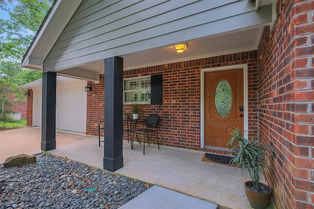 view of exterior entry featuring a porch, brick siding, and a garage