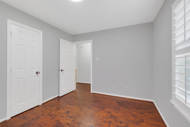 unfurnished bedroom featuring baseboards, multiple windows, and wood finished floors