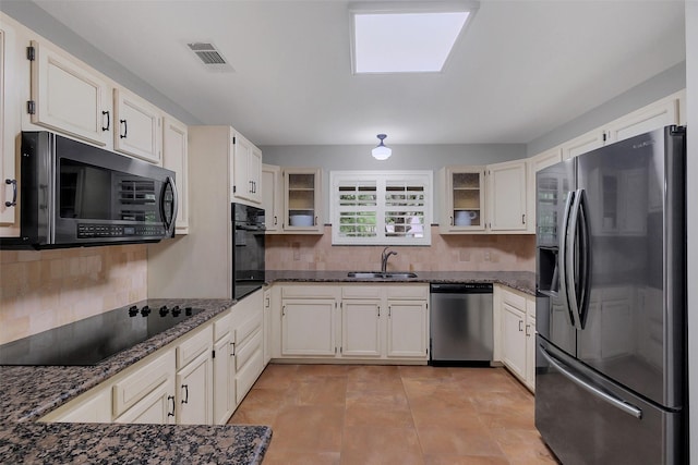kitchen featuring a sink, dark stone counters, black appliances, visible vents, and decorative backsplash