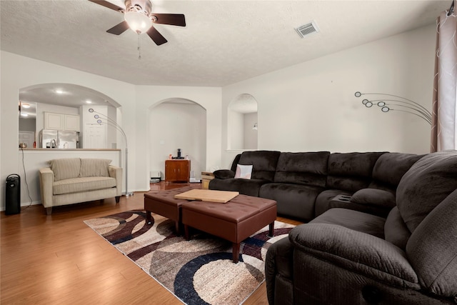 living room featuring arched walkways, wood finished floors, ceiling fan, and a textured ceiling