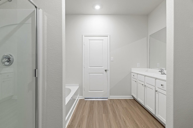full bath with a stall shower, baseboards, a bath, vanity, and wood finished floors