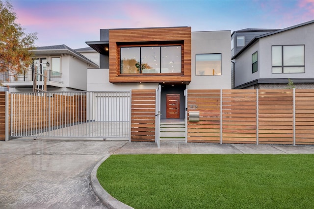 modern home with concrete driveway, a front yard, stucco siding, and fence