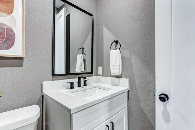 half bath with vanity, toilet, and a textured wall