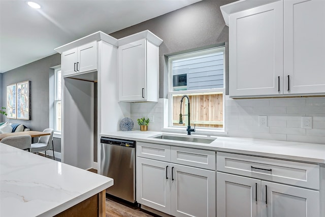 kitchen with a sink, dishwasher, backsplash, white cabinets, and light wood-style floors