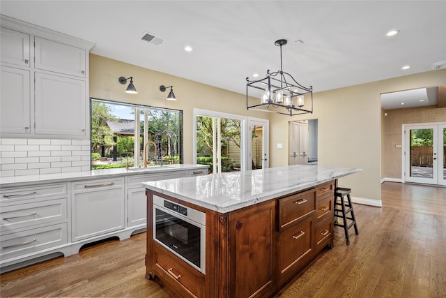 kitchen featuring a sink, white cabinets, wood finished floors, a center island, and a chandelier