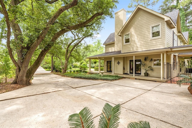 view of property exterior featuring covered porch, concrete driveway, a shingled roof, and a chimney