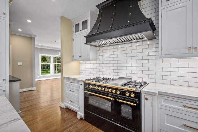 kitchen featuring premium range hood, double oven range, wood finished floors, decorative backsplash, and recessed lighting
