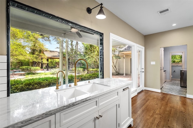 kitchen with a sink, ceiling fan, white cabinets, light stone countertops, and wood finished floors