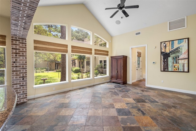 unfurnished living room featuring a ceiling fan, baseboards, stone tile flooring, and high vaulted ceiling