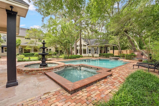 view of swimming pool featuring a pool with connected hot tub, fence, and a patio