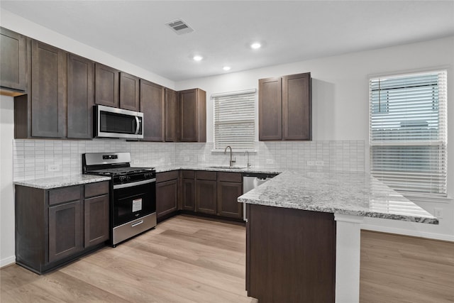 8114 Shelter Bay Ln, Cypress, TX 77433 - kitchen featuring dark brown cabinetry, a peninsula, stainless steel appliances, and light wood-style flooring