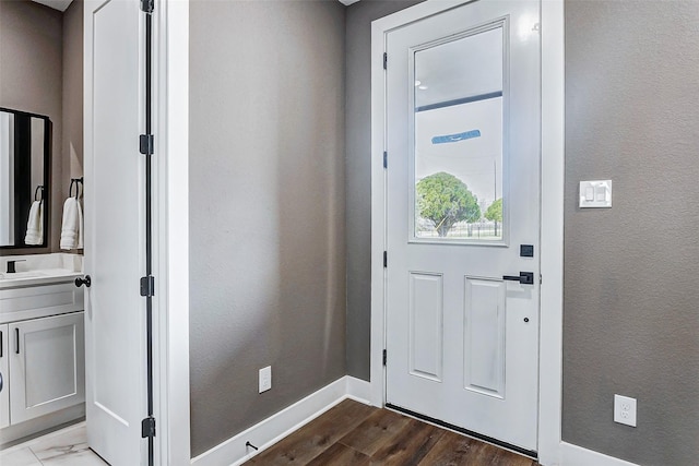 doorway to outside with baseboards, dark wood-style flooring, a sink, and a textured wall