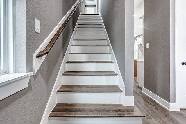 stairway with wood finished floors, baseboards, and a textured wall