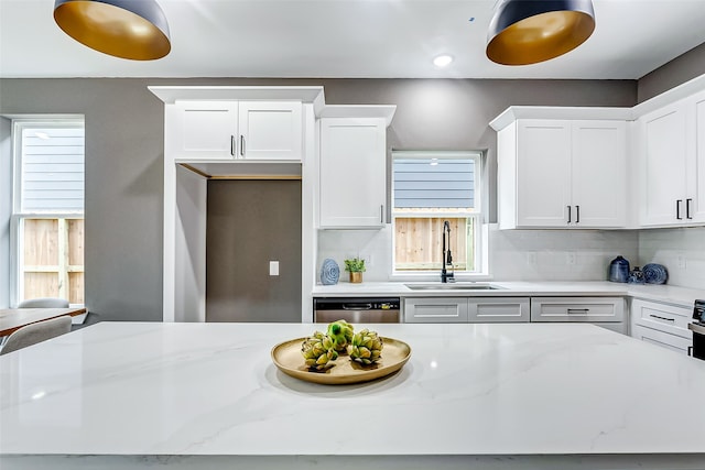 kitchen featuring a sink, white cabinets, stainless steel dishwasher, light stone countertops, and backsplash