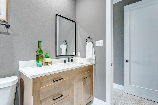 bathroom with toilet, baseboards, vanity, and a textured wall
