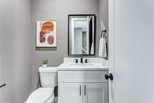 half bathroom featuring toilet, vanity, and a textured wall