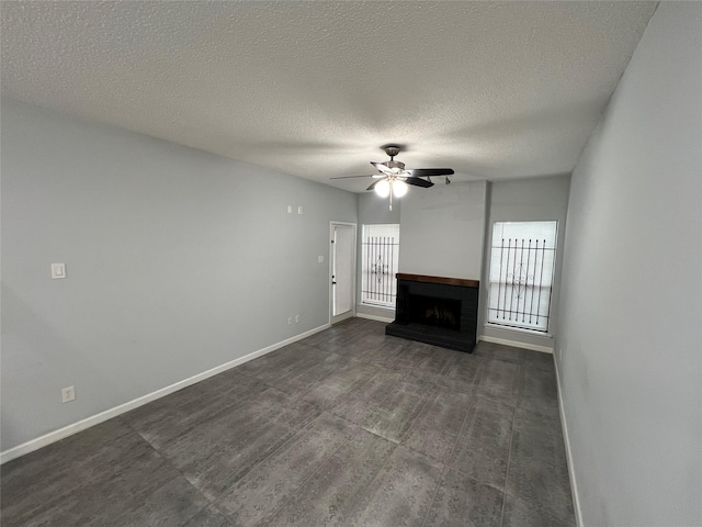 unfurnished living room with a ceiling fan, baseboards, a brick fireplace, and a textured ceiling