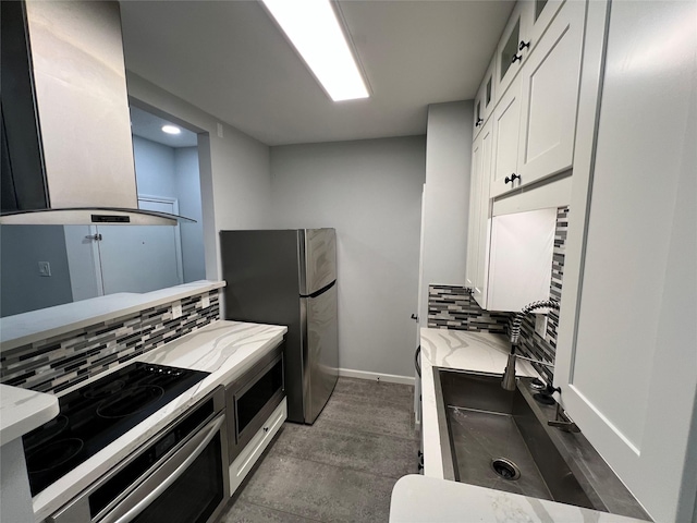 kitchen with appliances with stainless steel finishes, light stone counters, island range hood, white cabinetry, and decorative backsplash
