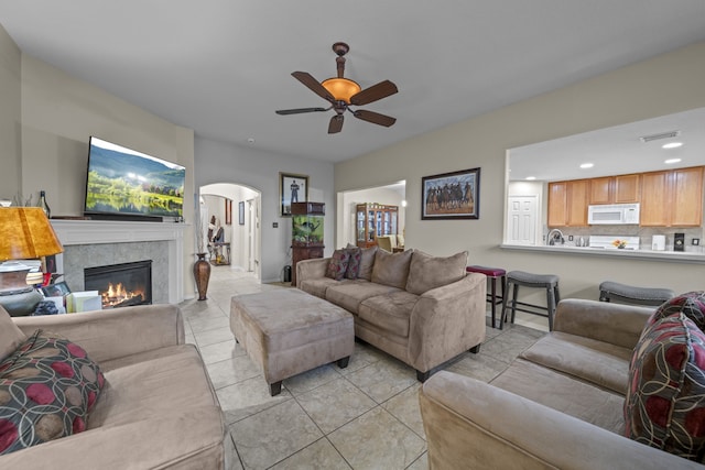 living area featuring light tile patterned floors, a ceiling fan, a tiled fireplace, arched walkways, and recessed lighting