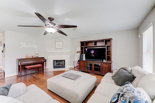 living area with wood finished floors, visible vents, a ceiling fan, baseboards, and a tiled fireplace