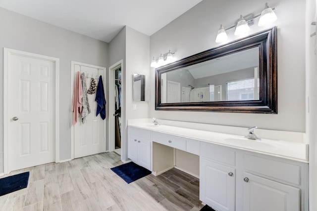 full bath with double vanity, a shower, wood finished floors, and a sink