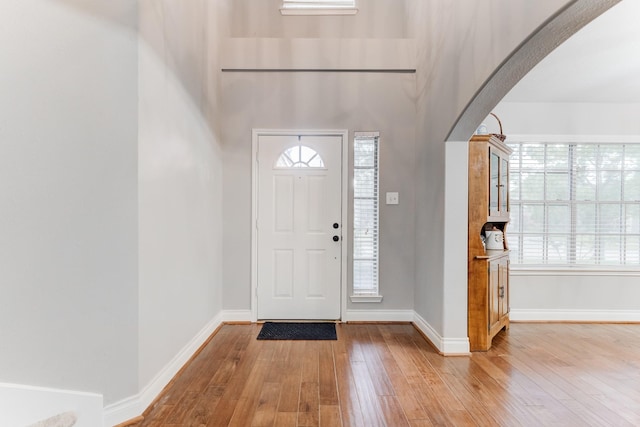 entrance foyer with light wood finished floors, arched walkways, and baseboards