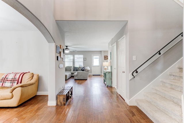 entryway with wood finished floors, a ceiling fan, arched walkways, and stairs