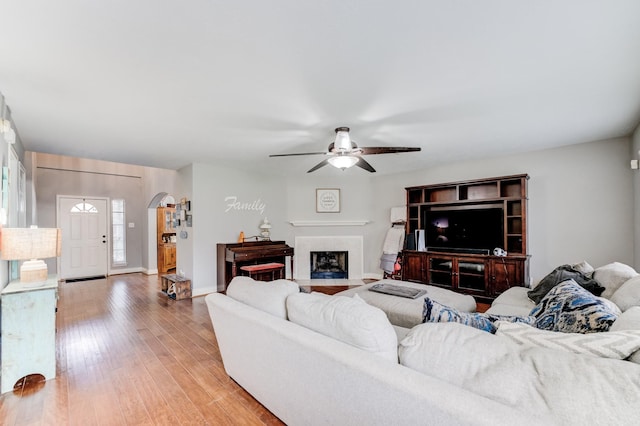living room with arched walkways, a ceiling fan, baseboards, a fireplace with flush hearth, and light wood-style floors