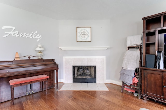 living area featuring a tile fireplace, baseboards, and wood finished floors