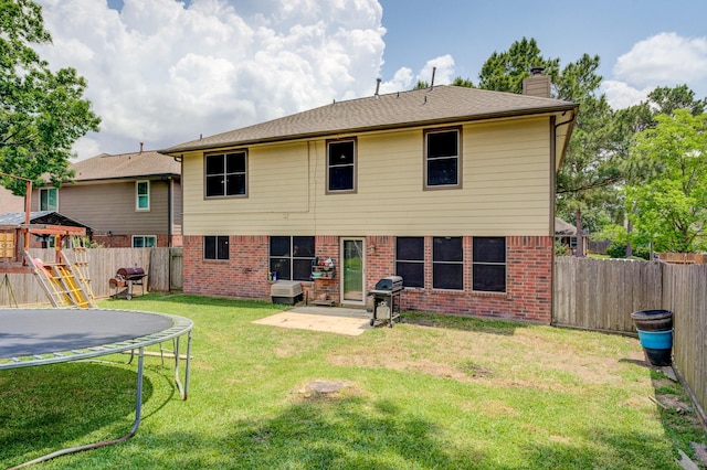 rear view of house featuring a trampoline, brick siding, a chimney, and a fenced backyard