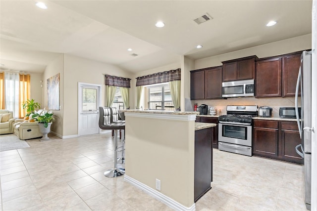 kitchen featuring stainless steel appliances, visible vents, light tile patterned floors, a kitchen island, and dark brown cabinets