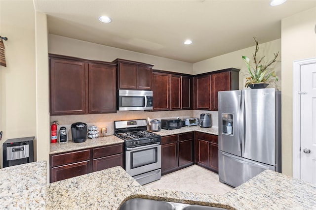 kitchen featuring appliances with stainless steel finishes, decorative backsplash, dark brown cabinets, and light stone countertops